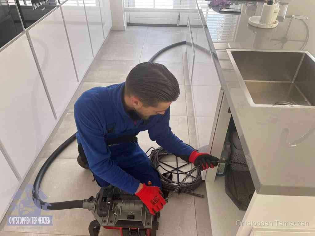 Een monteur ontstopt de keukenafvoer onder de spoelbak met een elektrische veermachine in Terneuzen Een monteur ontstopt de keukenafvoer onder de spoelbak met een elektrische veermachine in Terneuzen
