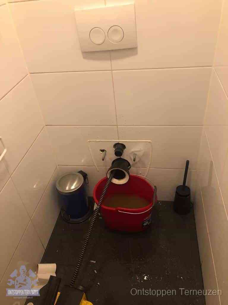 Een ontstopte wand-wc met verwijderde toiletpot waar een ontstoppingsveer in de wanduitgang verdwijnt, het achterhalen waar de verstopping zit in Terneuzen Een ontstopte wand-wc met verwijderde toiletpot waar een ontstoppingsveer in de wanduitgang verdwijnt, het achterhalen waar de verstopping zit in Terneuzen