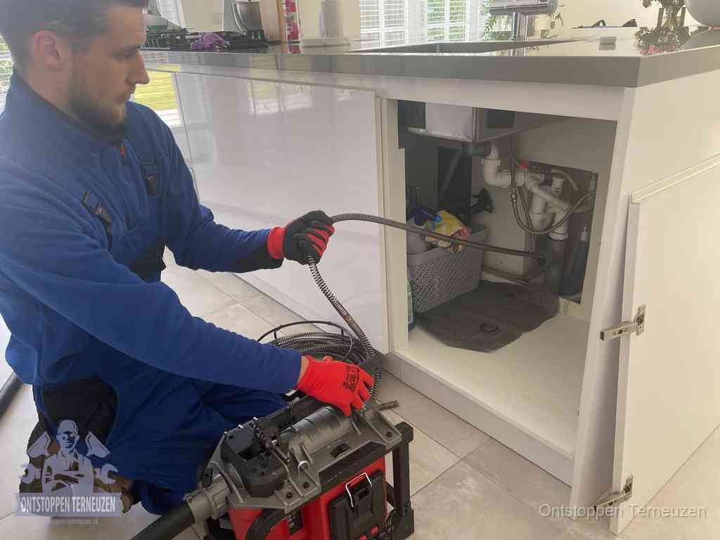 Monteur voert een ontstoppingsveer in de afvoer onder de keuken in Terneuzen Monteur voert een ontstoppingsveer in de afvoer onder de keuken in Terneuzen
