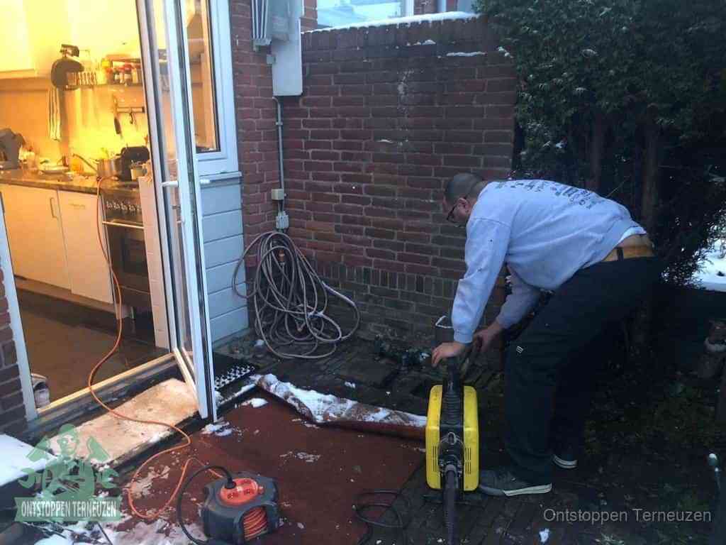 Een monteur werkt buiten bij een open riool-/grondput met een elektrische ontstoppingsmachine om een verborgen afvoerprobleem op te sporen in Terneuzen
