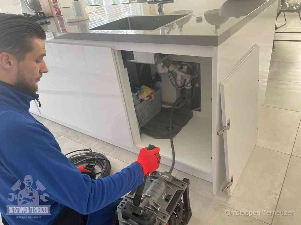 Monteur ontstopt met een veermachine een verstopte afvoer onder de gootsteen in Terneuzen Monteur ontstopt met een veermachine een verstopte afvoer onder de gootsteen in Terneuzen