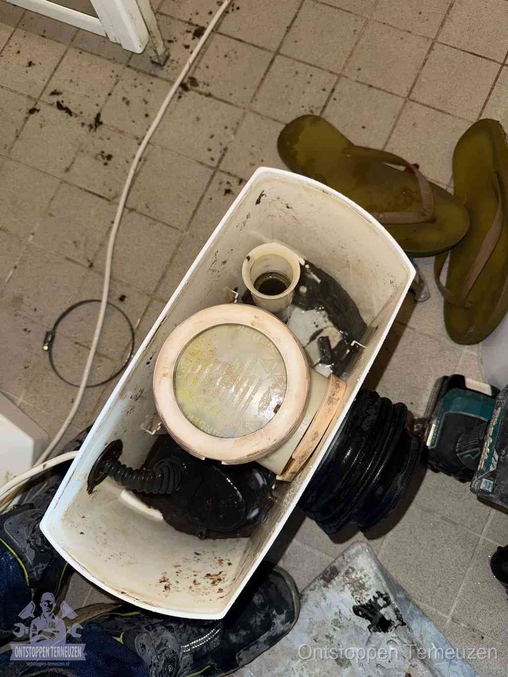 Een gedemonteerde toiletpot op de vloer met ontstoppingsveer en gereedschap ernaast, het verwijderen van een vastzittend voorwerp uit de wc in Terneuzen Een gedemonteerde toiletpot op de vloer met ontstoppingsveer en gereedschap ernaast, het verwijderen van een vastzittend voorwerp uit de wc in Terneuzen
