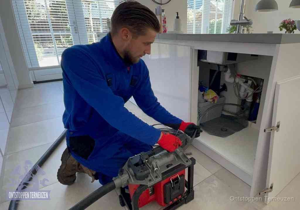 Een monteur voert een professionele elektrische ontstoppingsmachine in de afvoer onder de spoelbak tijdens het gootsteen ontstoppen in Terneuzen Een monteur voert een professionele elektrische ontstoppingsmachine in de afvoer onder de spoelbak tijdens het gootsteen ontstoppen in Terneuzen