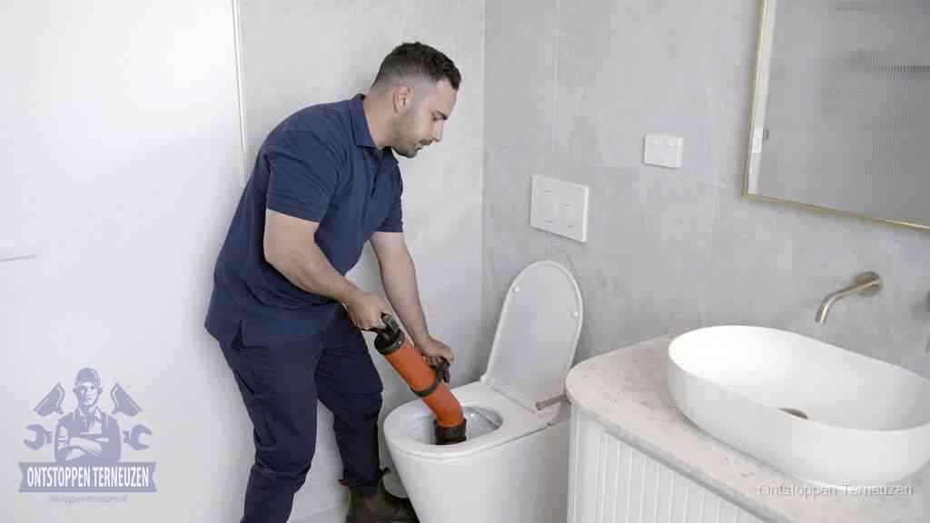 Een man gebruikt een handmatige luchtdruk-ontstopper in een modern betegeld toilet om zelf de wc te ontstoppen in Terneuzen Een man gebruikt een handmatige luchtdruk-ontstopper in een modern betegeld toilet om zelf de wc te ontstoppen in Terneuzen